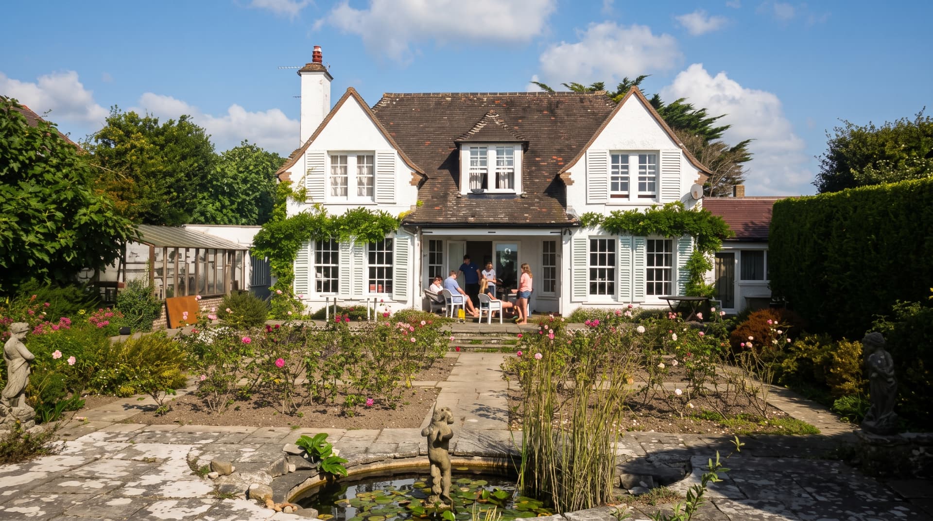 Blue Waters from the garden, with the pond and rose beds in the foreground and guests on the terrace